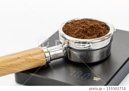 Close-up of metal portafilter filled with espresso coffee grounds on digital scale displaying weight measurement Close-up of metal portafilter filled with espresso coffee grounds on digital scale displaying weight measurement 133302718