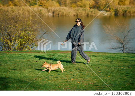 Smiling woman having fun walking and playing with her dog near lake 133302908