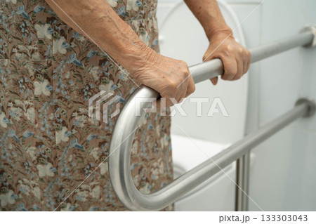 Asian elderly woman patient use toilet support rail in bathroom. 133303043