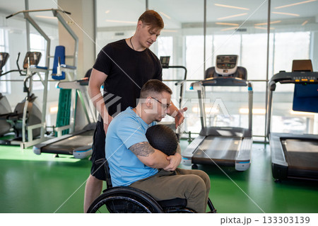 Disabled man doing workout with heavy med ball with help and guidance from personal trainer in gym. Disabled man doing workout with heavy med ball with help and guidance from personal trainer in gym. 133303139