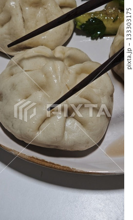 Steamed Chinese bao buns served on a plate with cucumber salad, picked up with wooden chopsticks. Concept of Asian cuisine, traditional comfort food and handmade dumplings 133303175