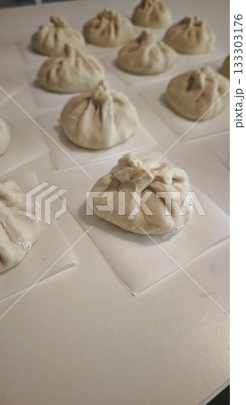 Uncooked homemade bao buns resting on parchment squares before steaming. Concept of traditional food preparation, Asian cuisine and handmade dumplings Uncooked homemade bao buns resting on parchment squares before steaming. Concept of traditional food preparation, Asian cuisine and handmade dumplings 133303176