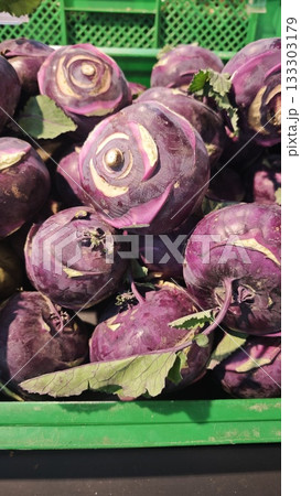 Fresh purple kohlrabies in a green plastic crate at an outdoor market, illuminated by natural sunlight. Concept of healthy eating, local farming and organic seasonal produce Fresh purple kohlrabies in a green plastic crate at an outdoor market, illuminated by natural sunlight. Concept of healthy eating, local farming and organic seasonal produce 133303179