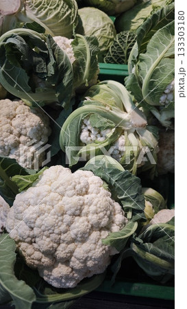 Fresh heads of white cauliflower with green leaves displayed in a market crate under natural light. Concept of organic farming, vegetarian food and seasonal local harvest 133303180