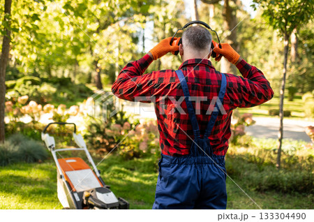Man standing in park holding headphones while working as gardener Man standing in park holding headphones while working as gardener 133304490
