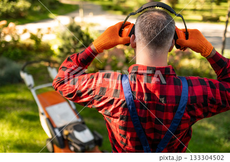 Landscaper touching hearing protection gear posing backwards Landscaper touching hearing protection gear posing backwards 133304502
