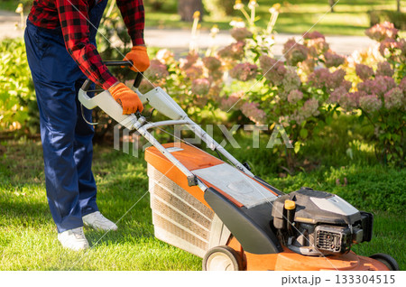 Groundskeeper on green grass working with mower equipment 133304515
