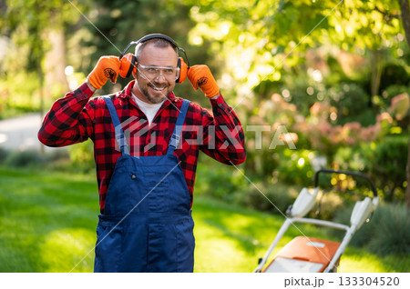 Male gardener adjusting protective earmuffs during lawn maintenance 133304520