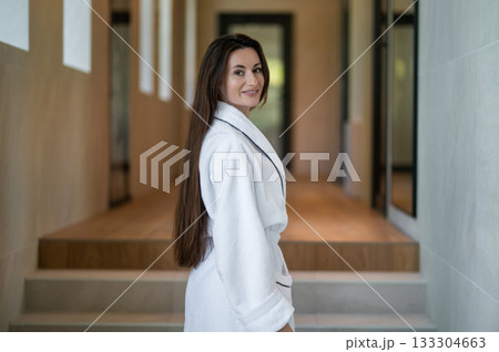 Beautiful young caucasian woman in white bath robe feeling contented and pleased 133304663