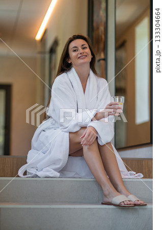 Beautiful young caucasian woman in white bath robe feeling contented and pleased Beautiful young caucasian woman in white bath robe feeling contented and pleased 133304664