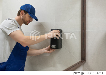 Worker fixing wall mounted soap dispenser in modern bathroom Worker fixing wall mounted soap dispenser in modern bathroom 133304751