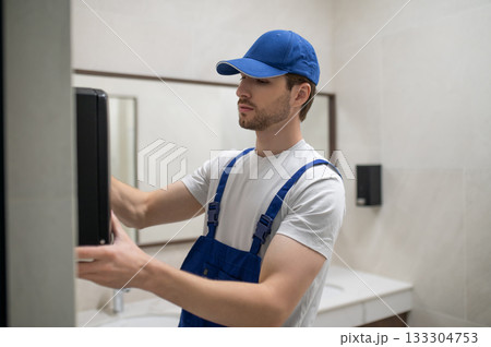 Maintenance technician installing new hand dryer on tiled wall 133304753