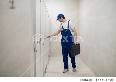 Plumber checking toilet cubicle door holding toolbox 133304756