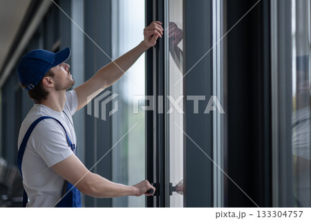 Male installer securing hinges and hardware on glass door 133304757