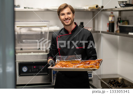 Chef in uniform holding metal tray with marinated food in kitchen Chef in uniform holding metal tray with marinated food in kitchen 133305341