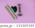 Jade massager and hairbrush on a pink background. Background with copy space. 133305395