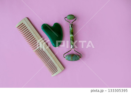 Jade massager and hairbrush on a pink background. Background with copy space. Jade massager and hairbrush on a pink background. Background with copy space. 133305395