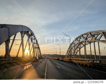 The metal structures of the road bridge in the rays of the setting sun 133306376