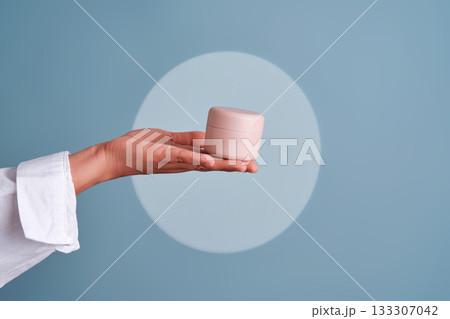 Hand presenting pink cosmetic cream jar for skincare 133307042