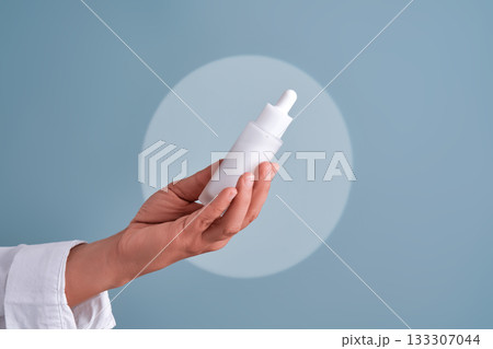 Hand holding white cosmetic dropper bottle 133307044