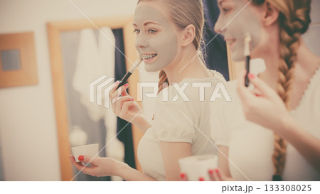 Happy young woman applying mud mask on face 133308025