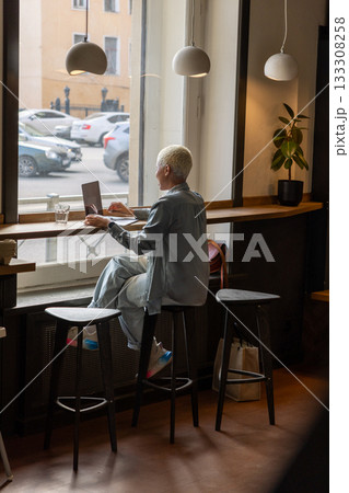 African American woman with short blond hair is sitting at a table, typing on laptop. 133308258