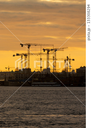 horizon with many construction cranes in sunset sky in background. sky is orange. 133308294
