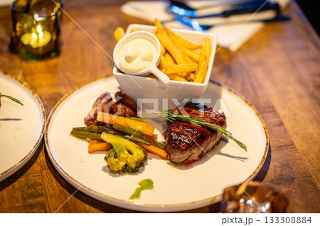 Breaded fried chicken breast with fries and onion rings, in a cardboard tray with wooden cutlery. Environmentally friendly disposable plastic free container 133308884