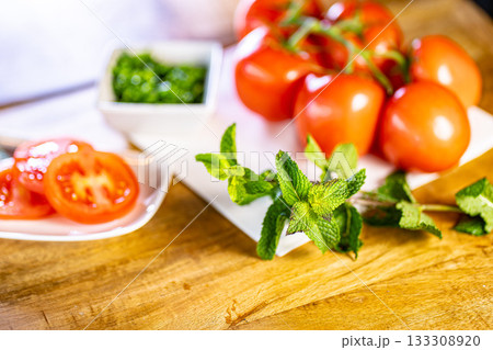 Red fresh tomatoes with mint and basil on wooden table over bokeh background 133308920