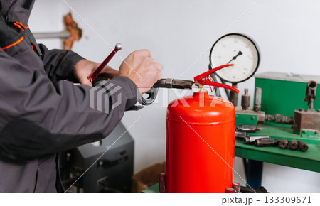 Technician refilling red fire extinguisher during pressure testing at workshop, close up 133309671