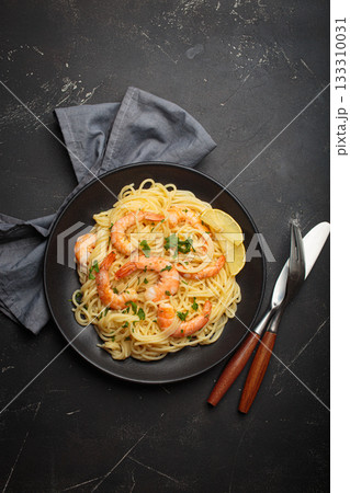 Spaghetti pasta shrimps parsley lemon seafood meal black plate dark background Spaghetti pasta shrimps parsley lemon seafood meal black plate dark background 133310031