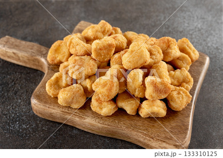 Golden crispy chicken popcorn on wooden cutting board against a gray background. Close-up. Fast food Golden crispy chicken popcorn on wooden cutting board against a gray background. Close-up. Fast food 133310125