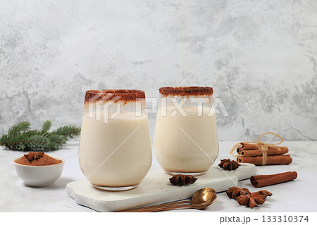 Eggnog with cinnamon, star anise, and nutmeg for Christmas and the winter holidays on a marble table with fir branches. A warming eggnog during the cold season, a festive arrangement for Christmas Eve 133310374