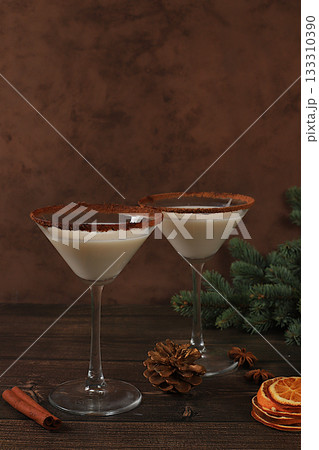 Christmas martini with cinnamon, nutmeg and dark chocolate on a background with fir branches, concept for Christmas and winter holidays. Warming milk drink during the cold season, selective focus. 133310390