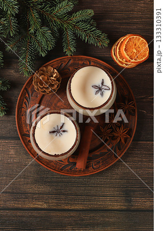A warming eggnog for the cold season, Eggnog with cinnamon, star anise, and nutmeg for Christmas and the winter holidays on a wooden table with fir branches. A festive arrangement for Christmas Eve 133310391