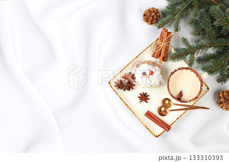 Eggnog with cinnamon and nutmeg for Christmas and winter holidays on a background of fir branches and decorations. Warming milk drink during the cold season, holiday composition, selective focus. Eggnog with cinnamon and nutmeg for Christmas and winter holidays on a background of fir branches and decorations. Warming milk drink during the cold season, holiday composition, selective focus. 133310393
