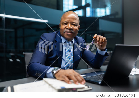 Mature black businessman holding glasses and looking at camera in modern office 133310471