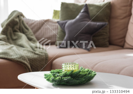 Cozy Living Room with Green Pillows, Knit Blanket, and Christmas Holiday Candle with Fir Wreath 133310494