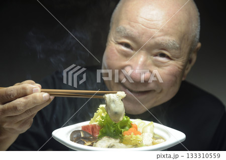 温かい牡蠣鍋を笑顔で食べる老人 133310559