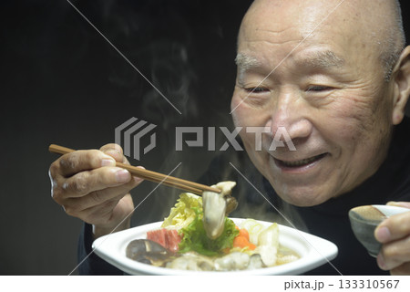 温かい牡蠣鍋を笑顔で食べる老人 133310567