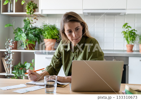 Concerned middle aged woman plans monthly expenses and income, checking financial stats on laptop. 133310673