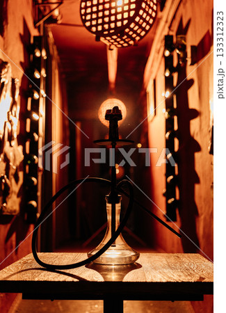 Hookah silhouette on wooden table under warm lights in moody lounge corridor 133312323