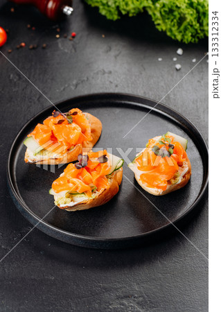 Top view of salmon canapes on baguette with cucumber and cream cheese on black plate 133312334