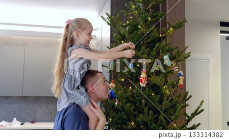 Heartwarming moment as father lifts his daughter onto his shoulders to help decorate Christmas tree. Father and daughter share special moment while decorating tree deep bond of family. Heartwarming moment as father lifts his daughter onto his shoulders to help decorate Christmas tree. Father and daughter share special moment while decorating tree deep bond of family. 133314382