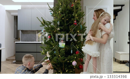 Smiling parents and child hanging ornaments, arranging twinkling lights on christmas tree, sharing warm seasonal moments together at home Smiling parents and child hanging ornaments, arranging twinkling lights on christmas tree, sharing warm seasonal moments together at home 133314398