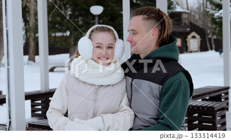 Winter landscape revealing affectionate young couple cuddling, wearing cozy outerwear, sharing intimate embrace amid snow covered park scene Winter landscape revealing affectionate young couple cuddling, wearing cozy outerwear, sharing intimate embrace amid snow covered park scene 133314419