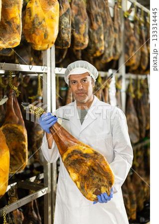 In jamon production shop, man employee demonstrates final product 133314445