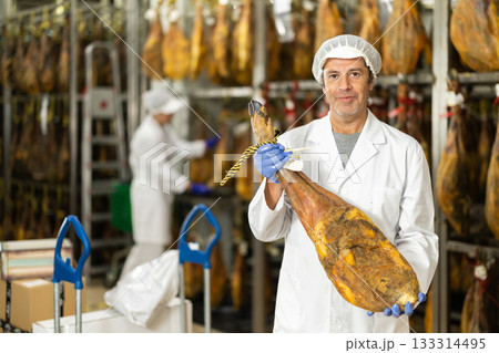 In jamon production shop, man employee demonstrates final product 133314495