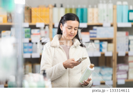 Middle-aged woman scanning QR-code on shampoo in drugstore Middle-aged woman scanning QR-code on shampoo in drugstore 133314611