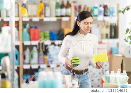 Woman in light clothes choosing sponges to wash dishes in supermarket 133314621
